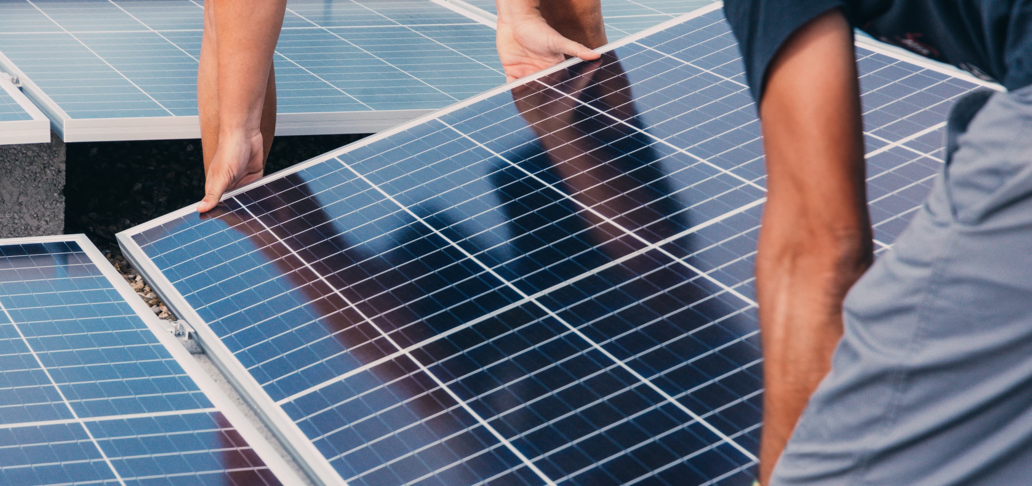 Two installers lifting a solar panel into place on a roof
