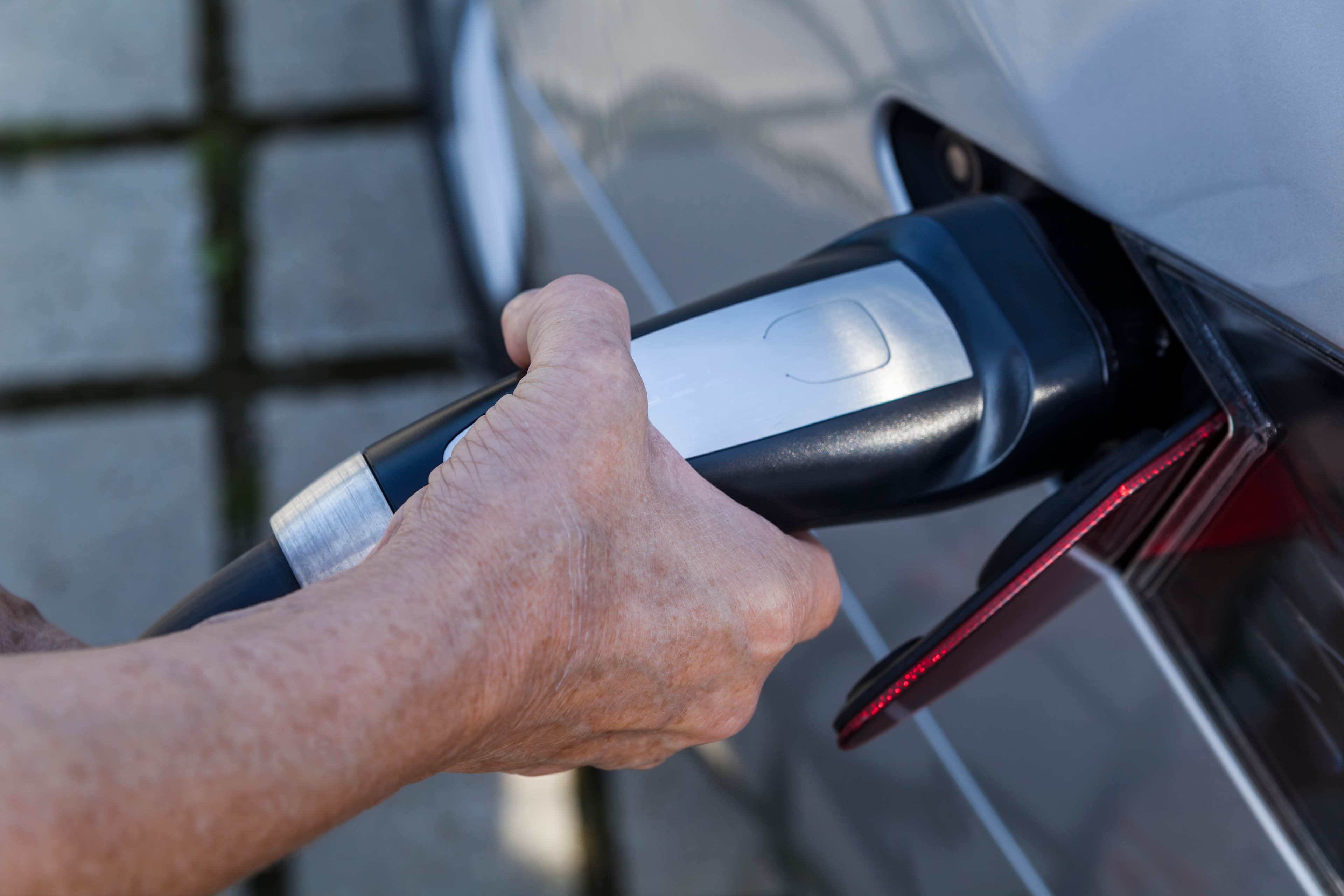 A hand plugging a Type 2 EV charging connector into the side of an electric car at home.