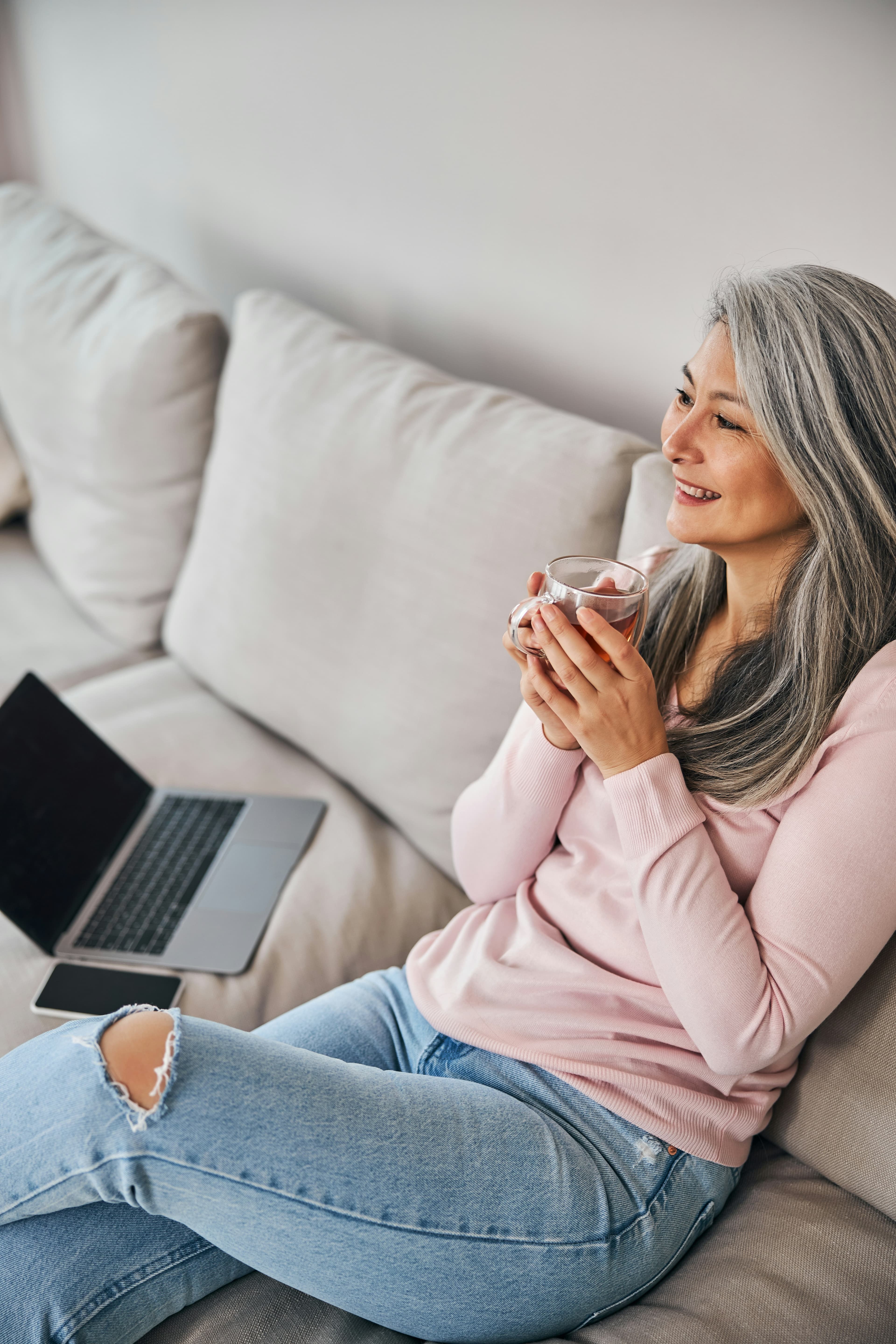 A woman relaxing on a sofa with coffee and a laptop, calm and unworried.