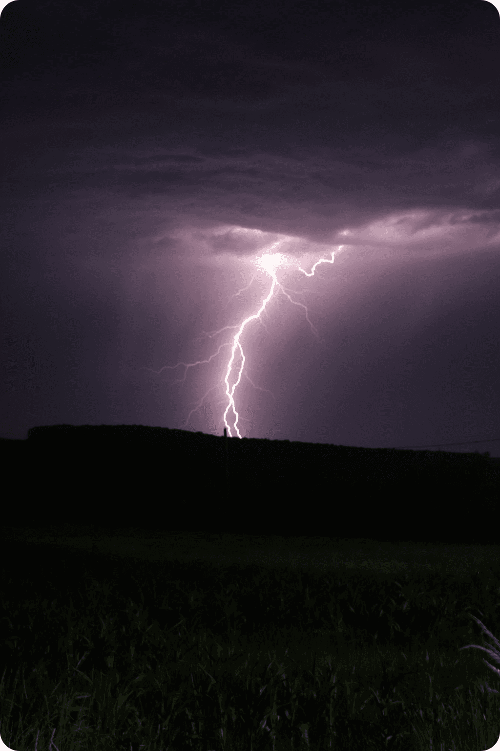 Lightning striking near a residential street at night, the kind of grid-side surge event the Basis SPD cartridge clamps before it reaches household appliances.